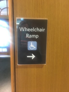 Sign (without Braille) signifying location of wheelchair ramp at east entrance of Thompson Library.